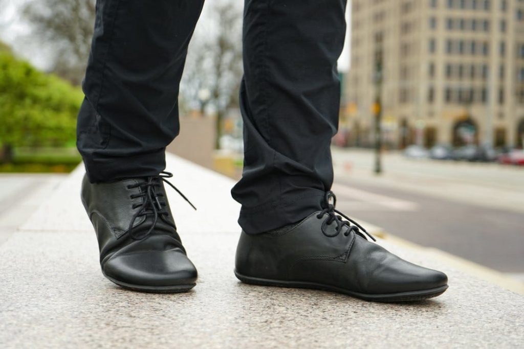 a person walking in elegant pants and vivobarefoot barefoot dress shoes in the street