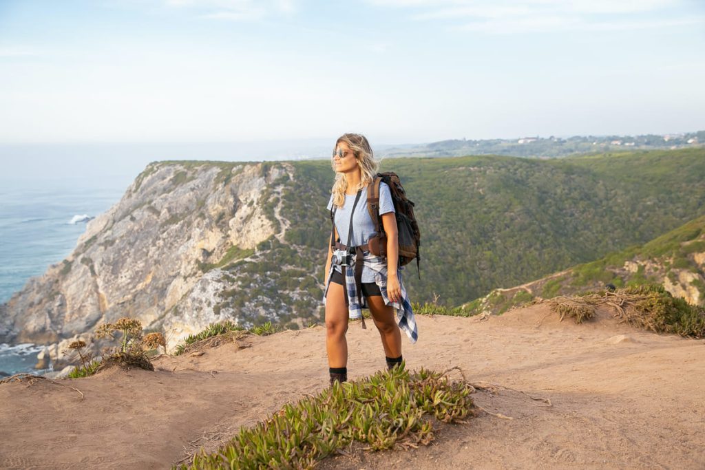 a woman hiking on cliff with mountains and the sea in the background